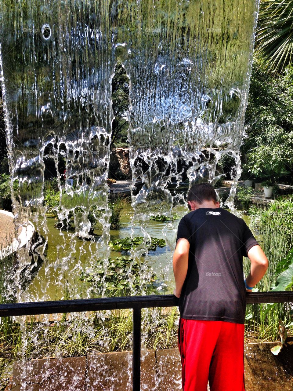 Staying cool. Boy leaning over in a waterfall at an outdoor garden exhibit 