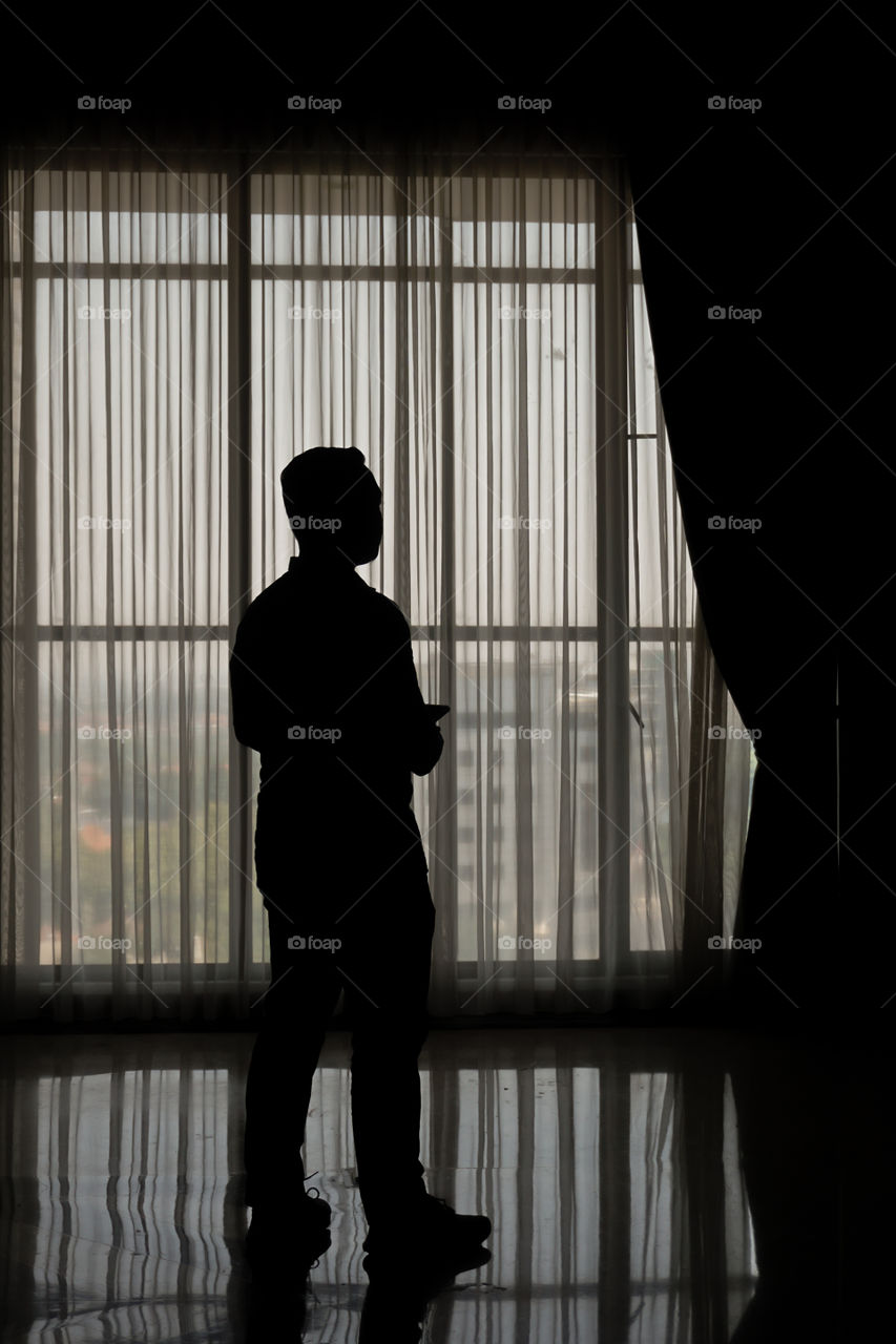 The silhoutte of a man standing in front of window.