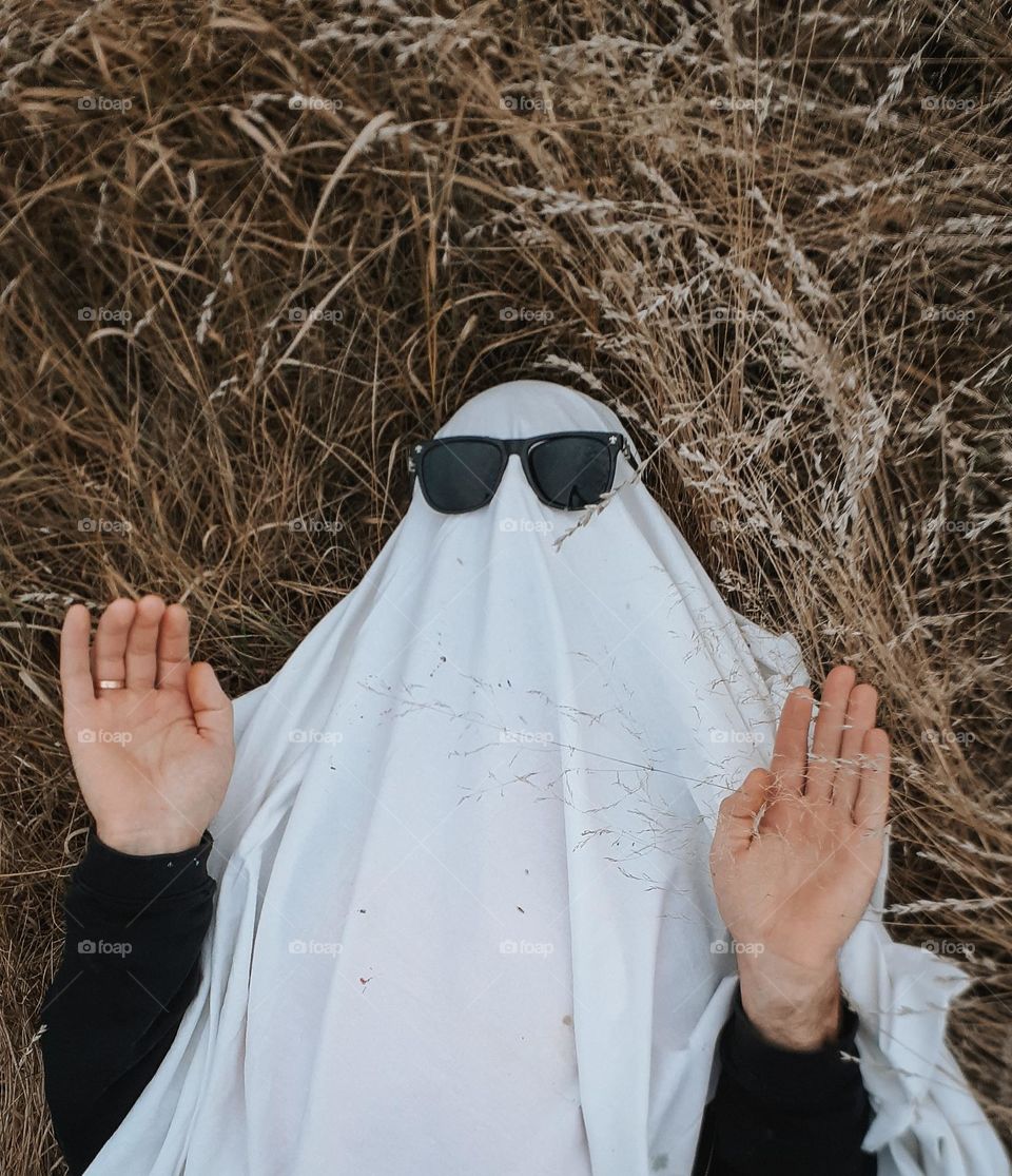 a man in a ghost Halloween costume lies among the dry autumn grass