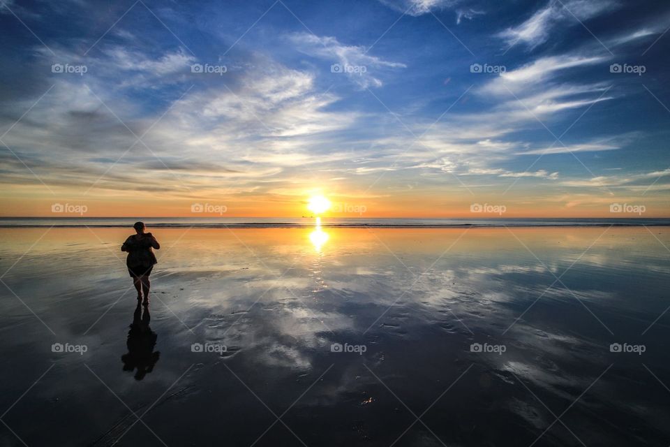 Person walking on sunset and sky reflected water