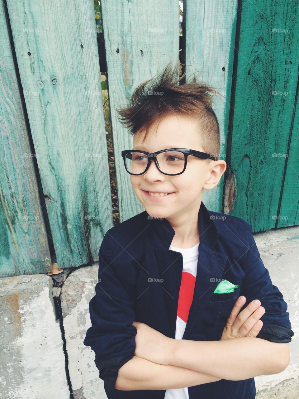 Cute little boy wearing eyeglasses and standing against wooden plank