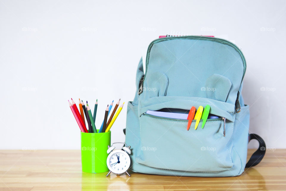 a funny school briefcase with markers, pencils and an alarm clock on the table.
