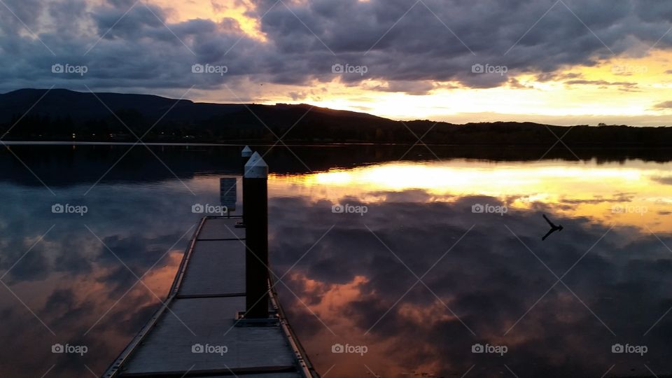 dark Sunset with dramatic clouds reflected in lake and empty dock