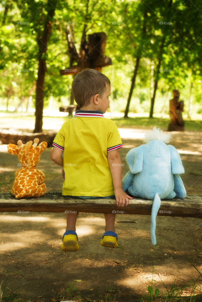 Little boy with a plush friends sitting on a bench in the park