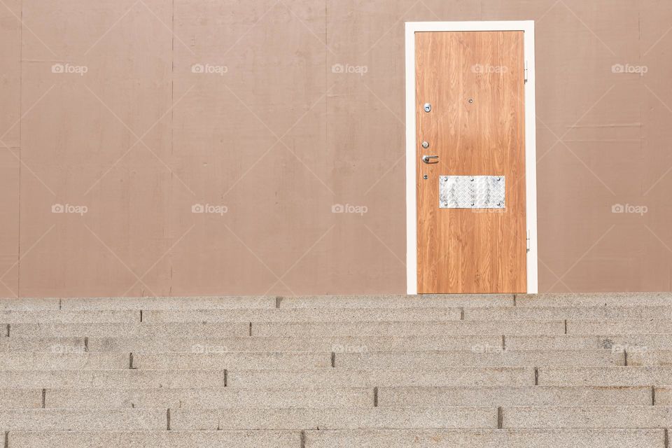 Steps leading to a wooden door on a brown beige wall 