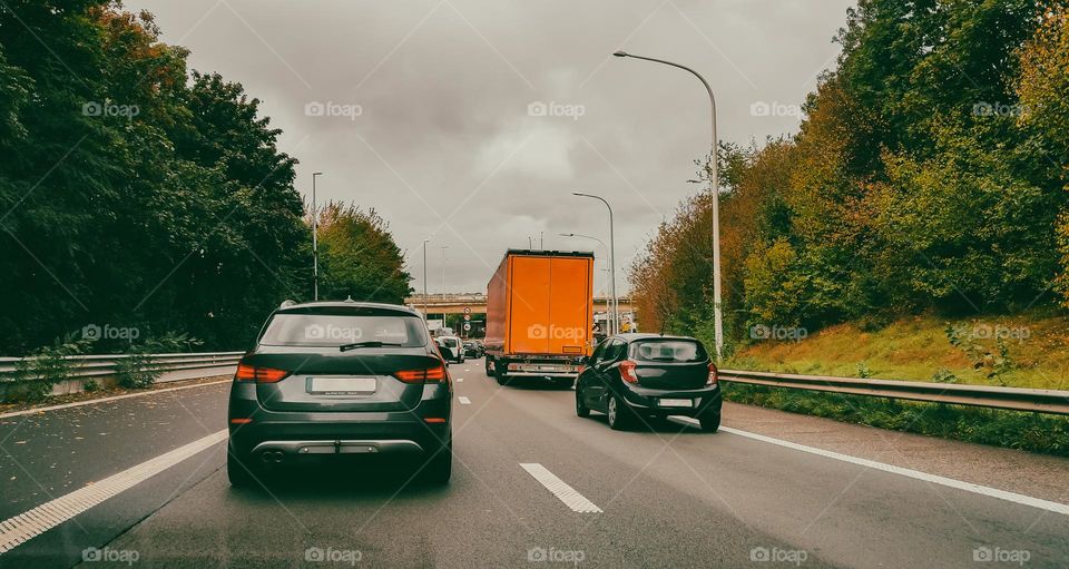 A beautiful view of the cars ahead with an orange truck on the European autobahn on an autumn rainy evening, close-up side view.