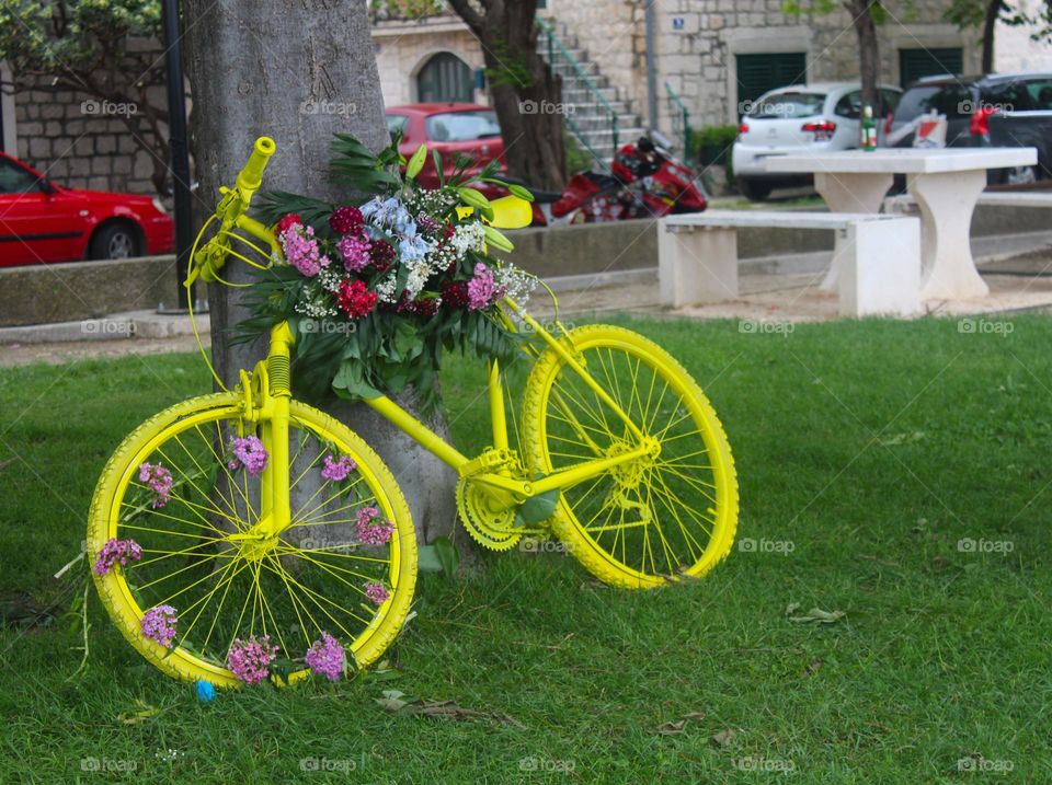 Beautiful yellow bicycle in public park decorated with flowers.  Spring city scape