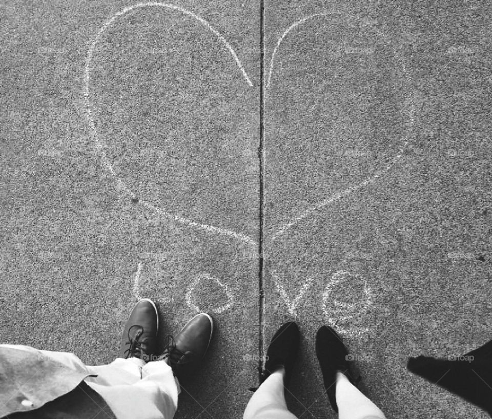 Black and white photo of a couple standing by a heart and the word 'love'. Sidewalk chalk and shoes.
