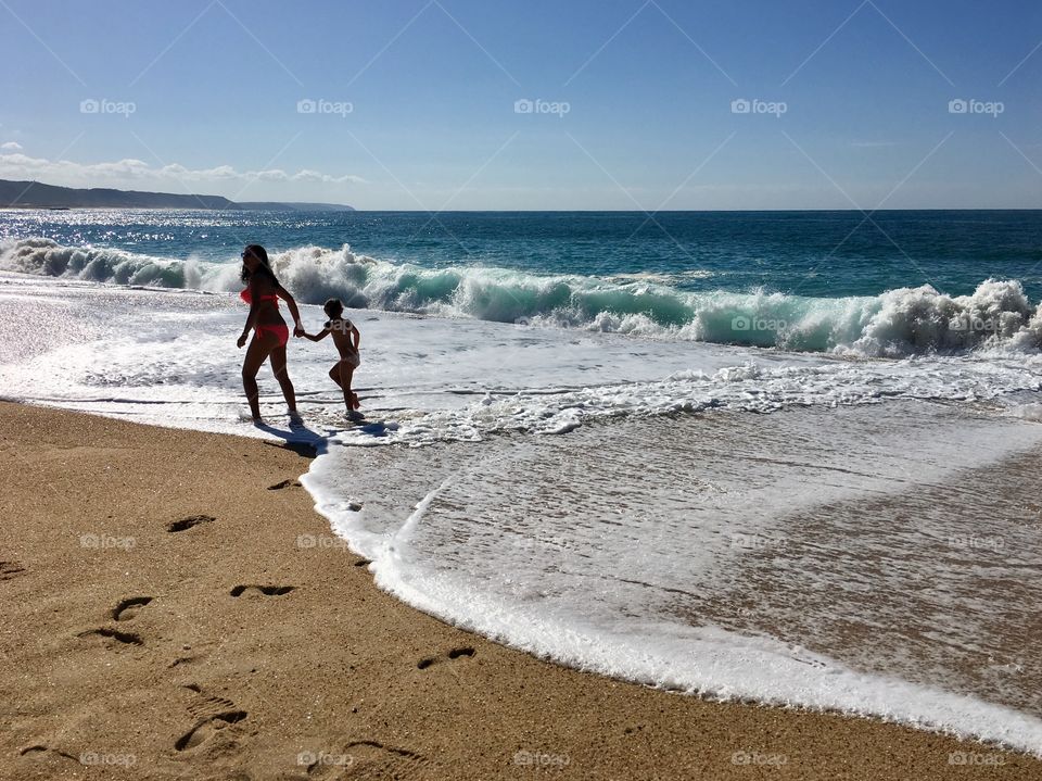 A woman enjoys the warm day at the beach with her daughter. 