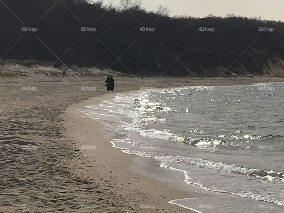 Two nuns walking on the beach near the glistening water.