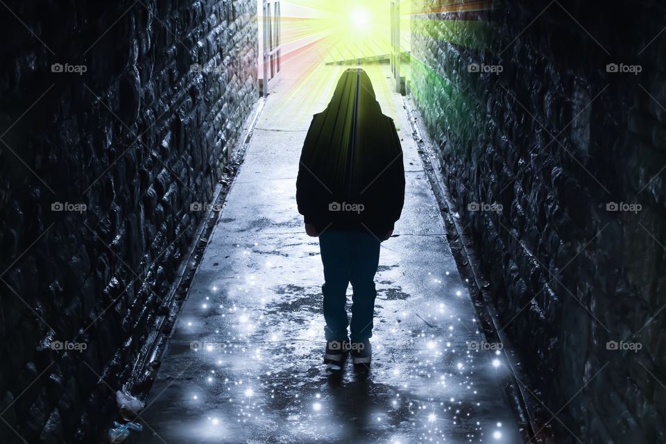 Hooded silhouetted boy walking into the light at the end of a tunnel