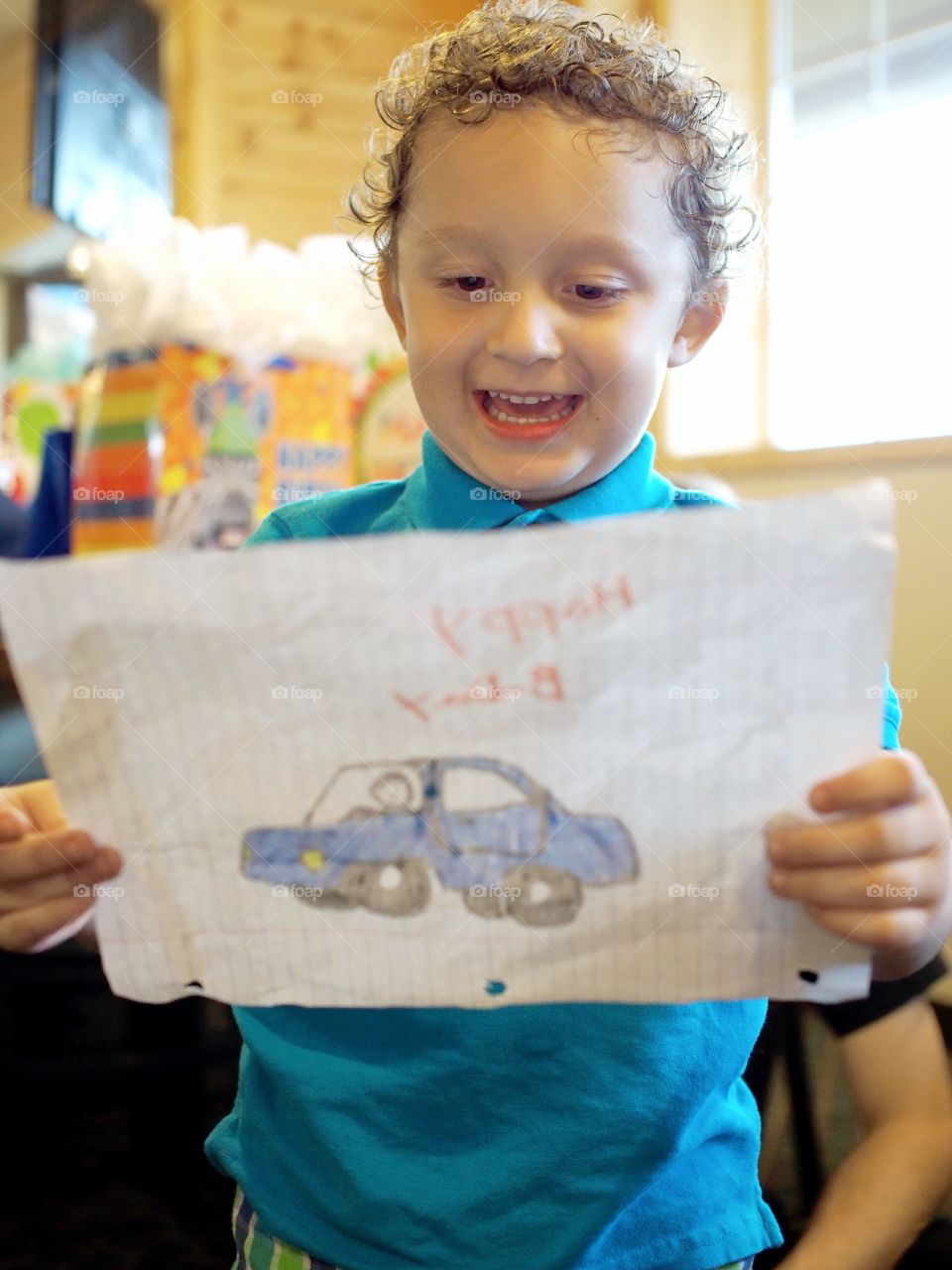 A young boy laughing joyfully from a handmade gift he received at his birthday party. 