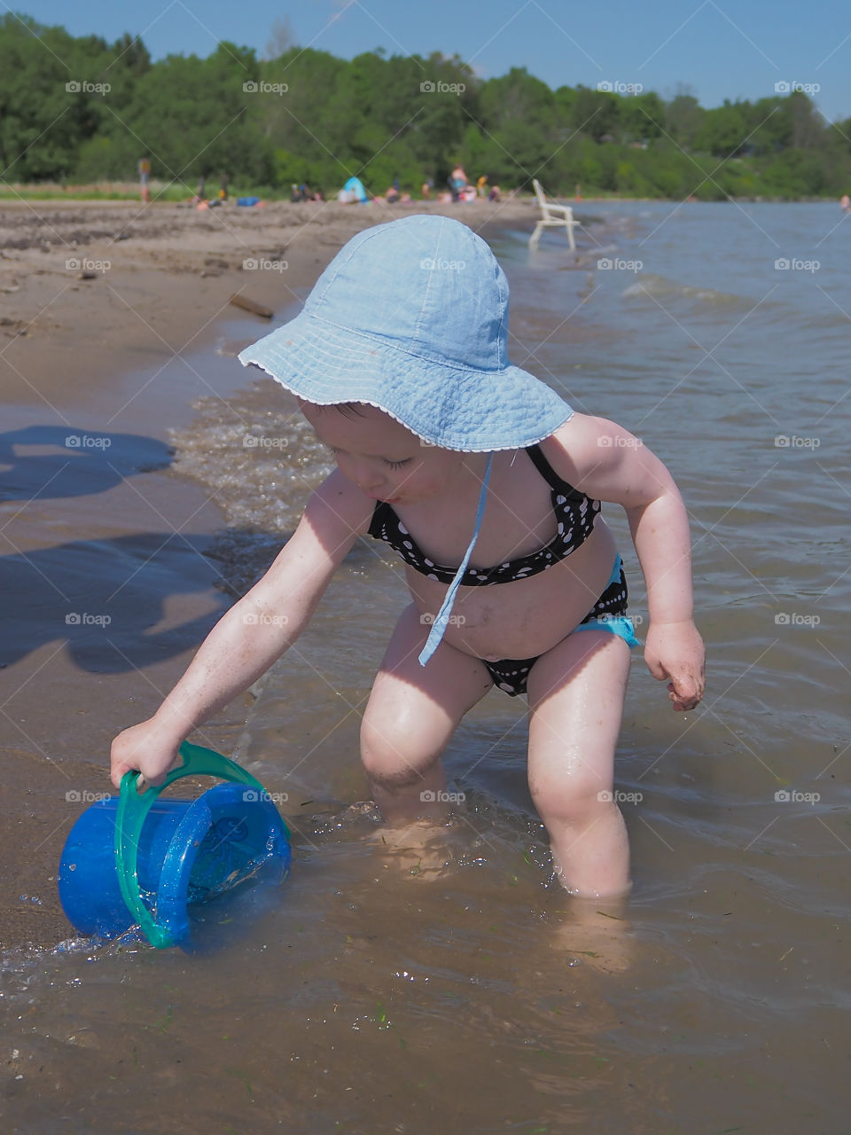 Toddler girl filling her blue bucket with water at the beach.