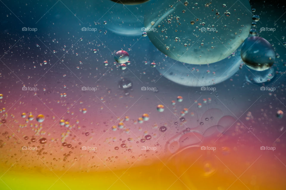 Bubbles of vegetable oil in clear water on a glass and transparent lid from a frying pan on colored paper.