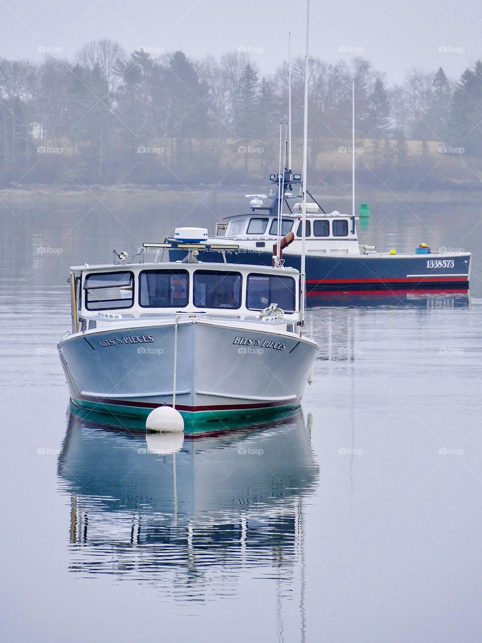 Two lobster boats are reflected in the still waters of a misty morning.