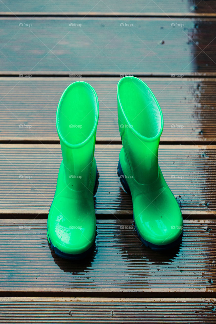 Row of wellies in various sizes standing on a wooden porch while raining