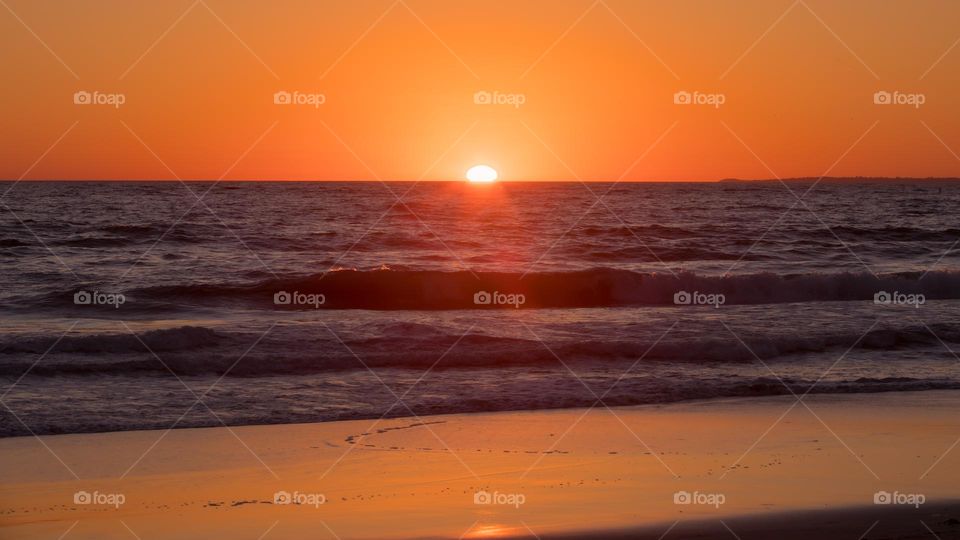 Sun setting into water horizon at Santa Monica Beach in Los Angeles, California, USA. Warm orange light from the sun reflect onto sea surface. April 2022.