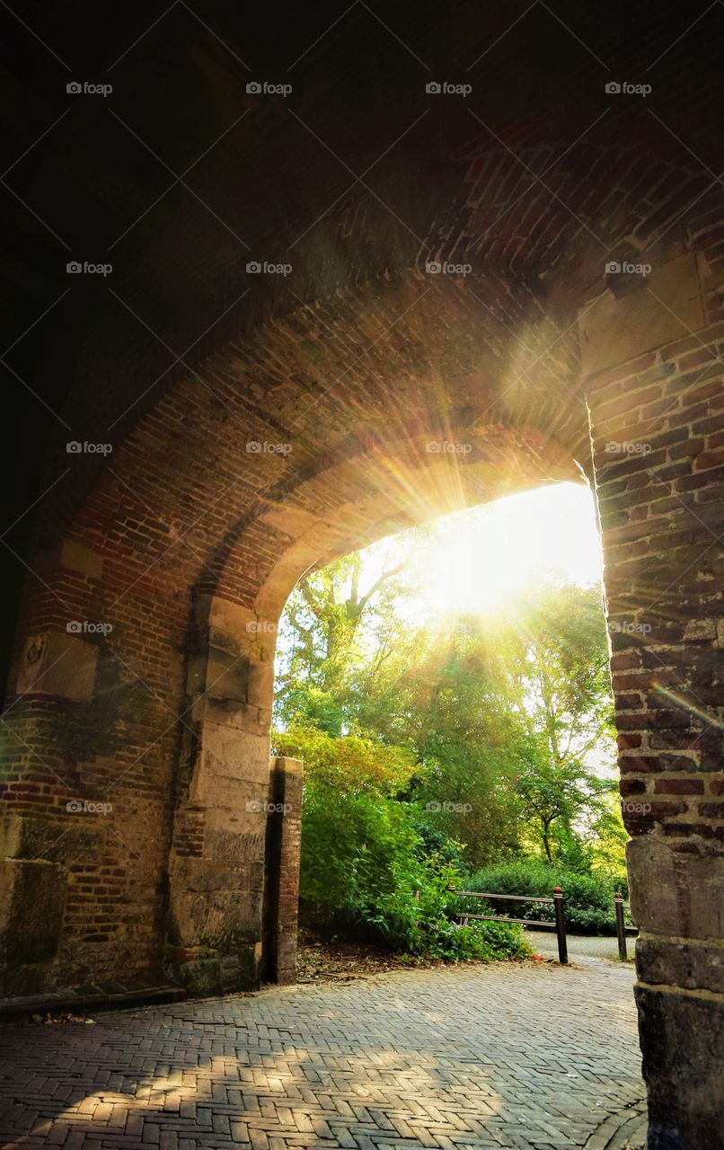 historical brick gate with sun rays shining trough the trees