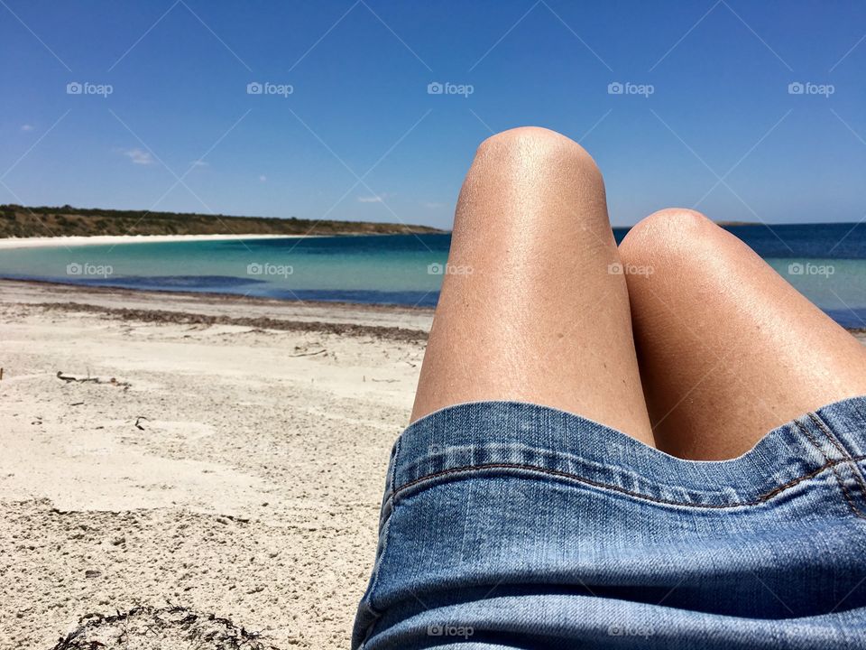 Taking it all in on a remote beach in south Australia. Woman in denim jean skirt and bare tanned legs laying on white sand beach, lower half of body only 