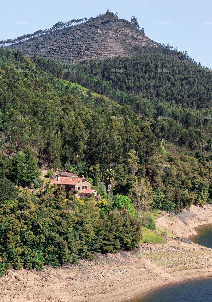 A stone lodge sits beneath a large hill and on the banks of the Rio Zêzere, near Dornes in Central Portugal 