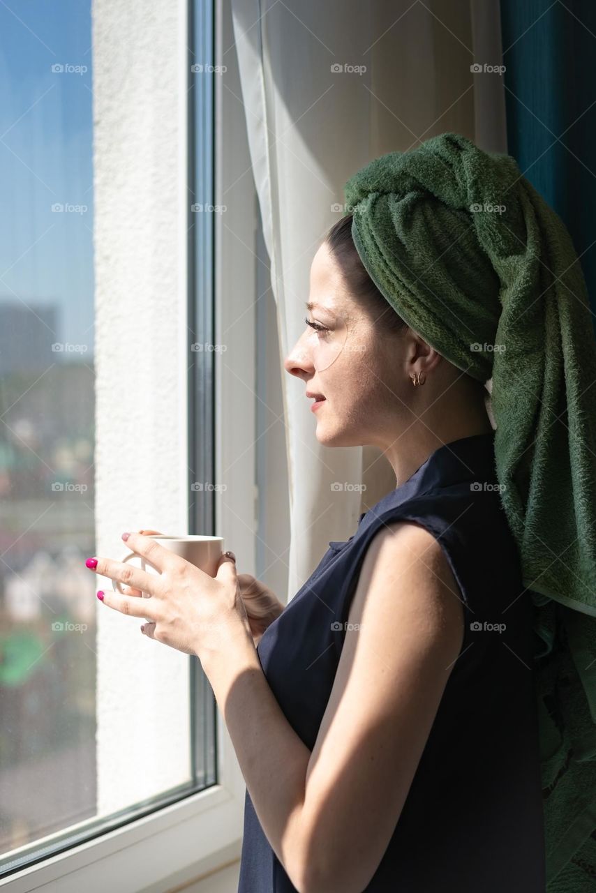Home beauty salon woman after a shower with patches on her eyes looking out the window