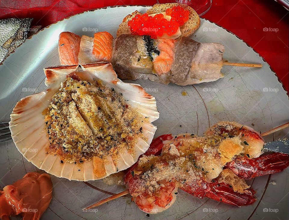 Italian food.  Galician scallop, lobster with sauce, grilled pieces of sea fish and white bread with red caviar on the plate