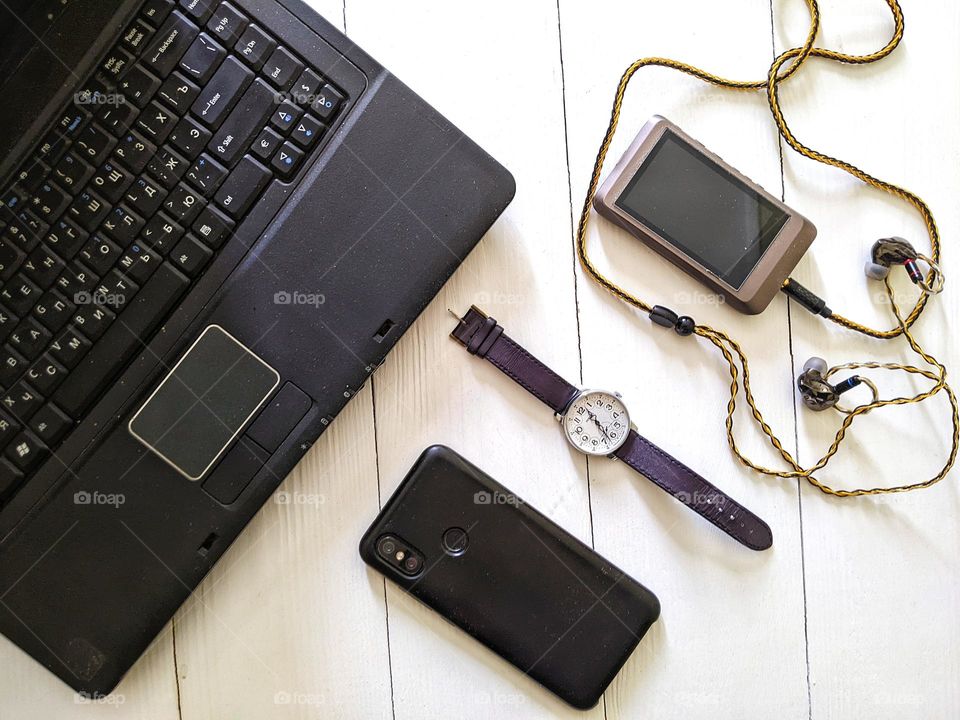 laptop, smartphone, music player with headphones, men's watch on a leather strap on a white background