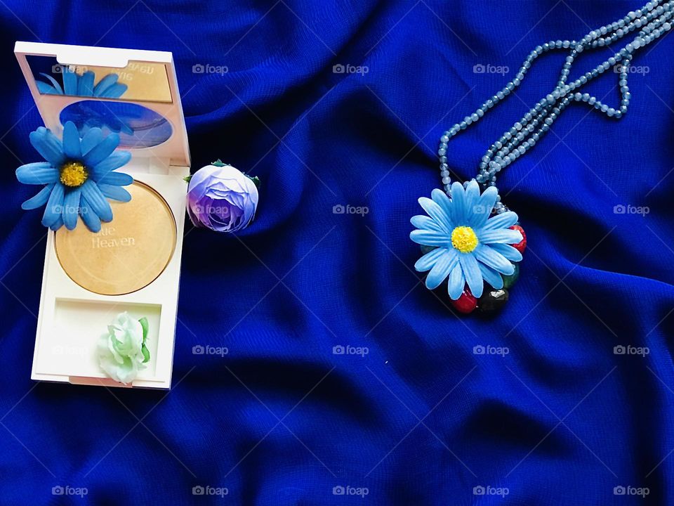 Blue heaven foundation powder along with blue flowers and beads garland on blue satin cloth 