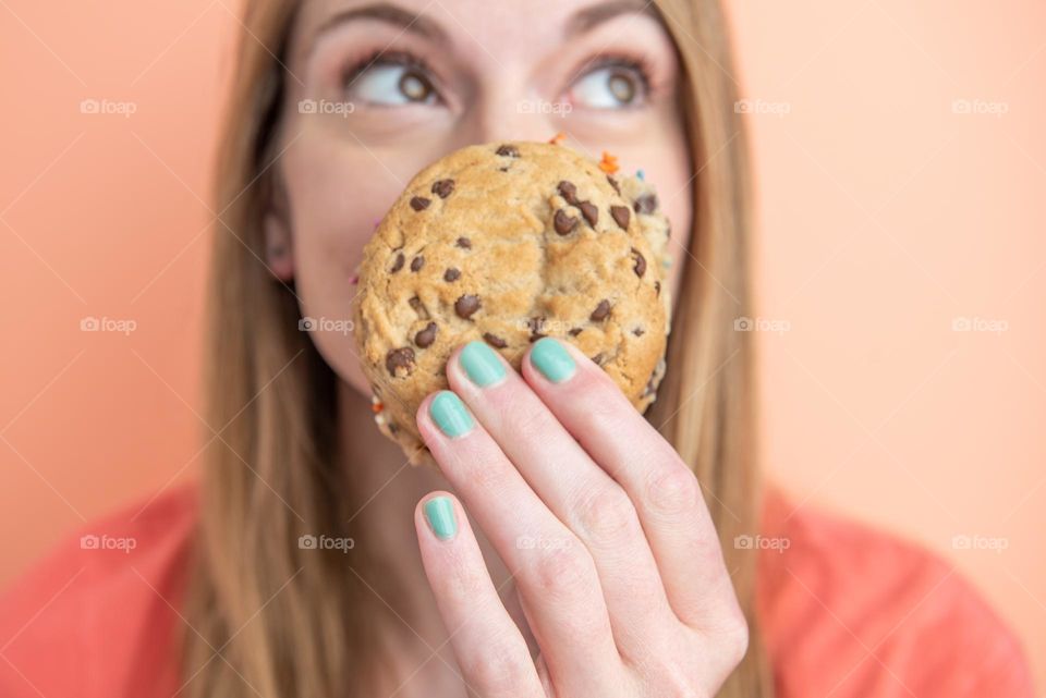 Fun portrait product shot of a young woman holding a chocolate chip cookie sandwich in front of her face 