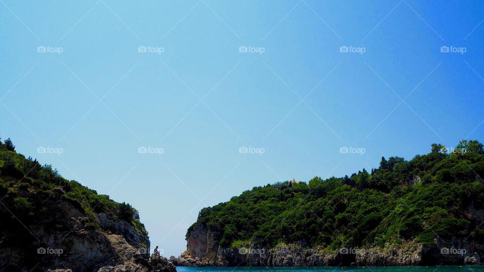 Paleokastritsa beach view with person perched on rock, Corfu, Greece