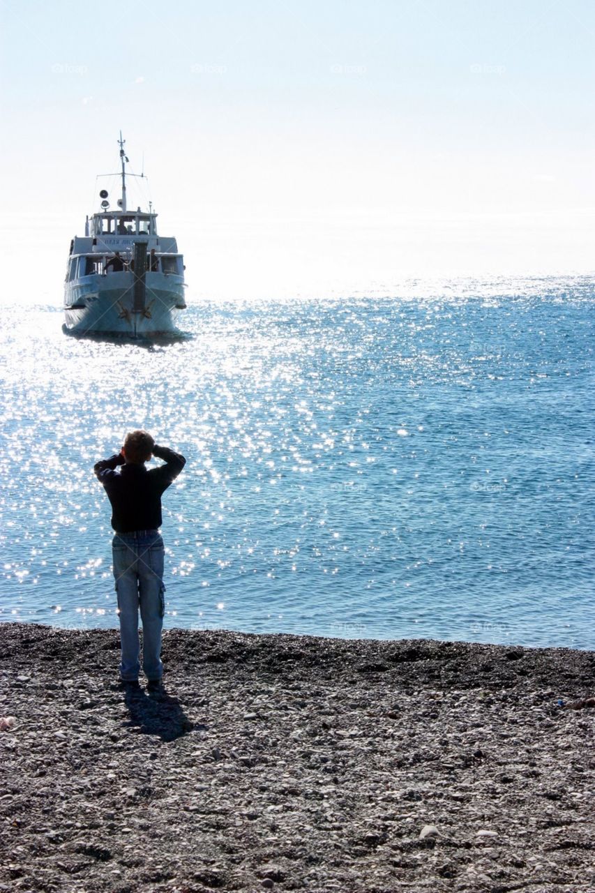 Boy looking at the ferry in the far sea 