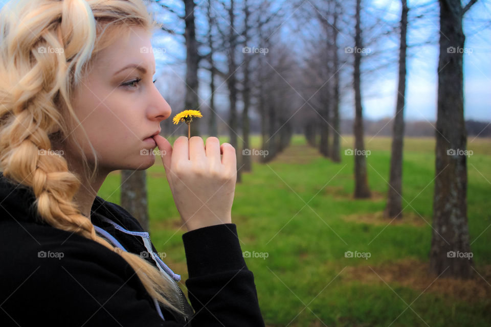 Young blonde girl holding flower against bare trees