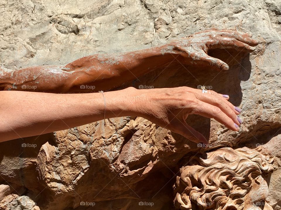 Female arm and hand stretched out beside sculpted aboriginal arm and hand 