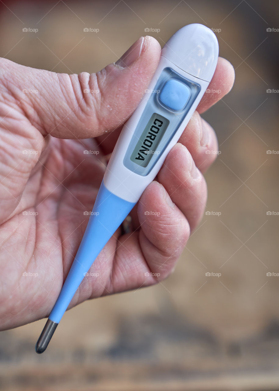 Male hand holds clinical thermometer with covid-19 text on the screen during global covid-19 or corona pandemic.