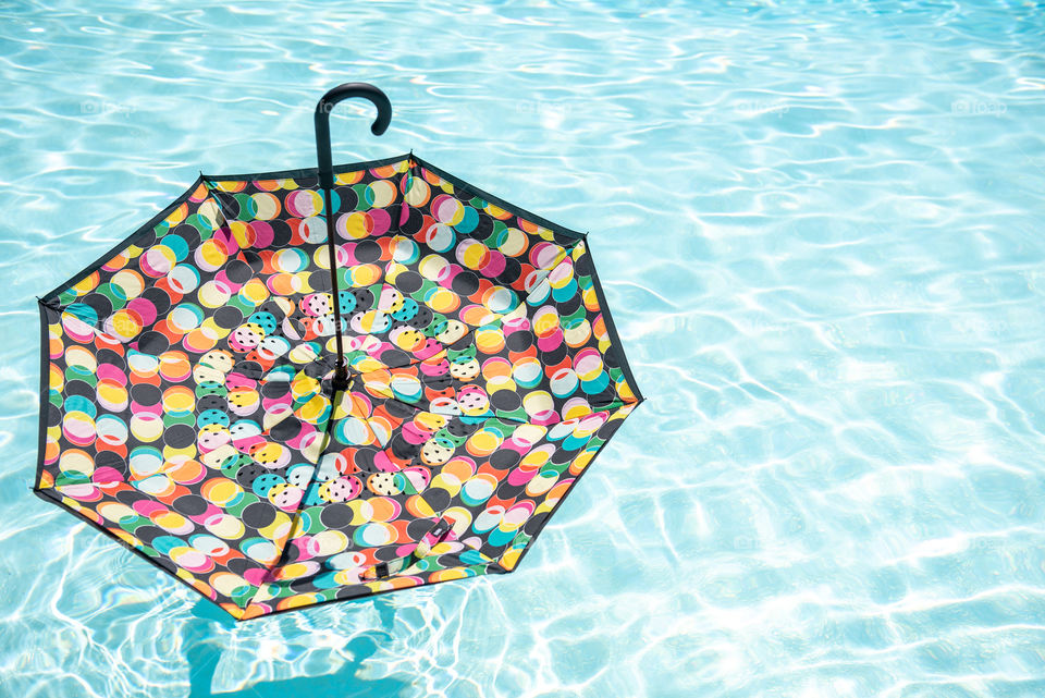 Colorful spotted umbrella floating on top of an outdoor swimming pool
