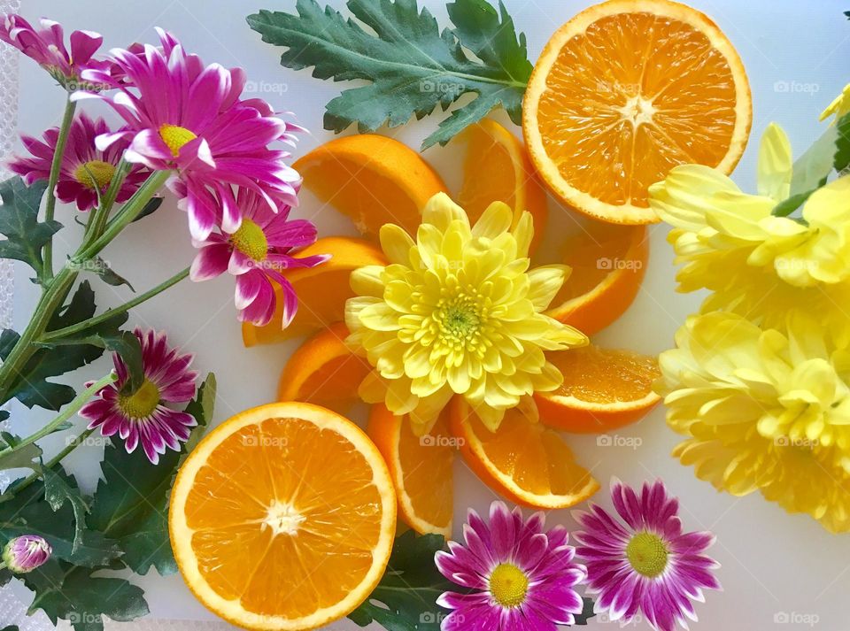 Summer treats flat lay: Fresh orange juice and wedges with fresh chrysanthemum and daisies