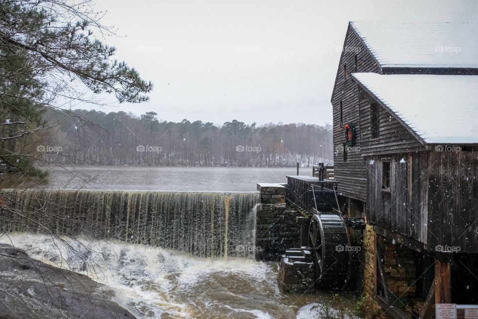 A festive view of the old rustic water mill and waterfall as snow falls during the Christmas season at Historic Yates Mill County Park in Raleigh North Carolina. 