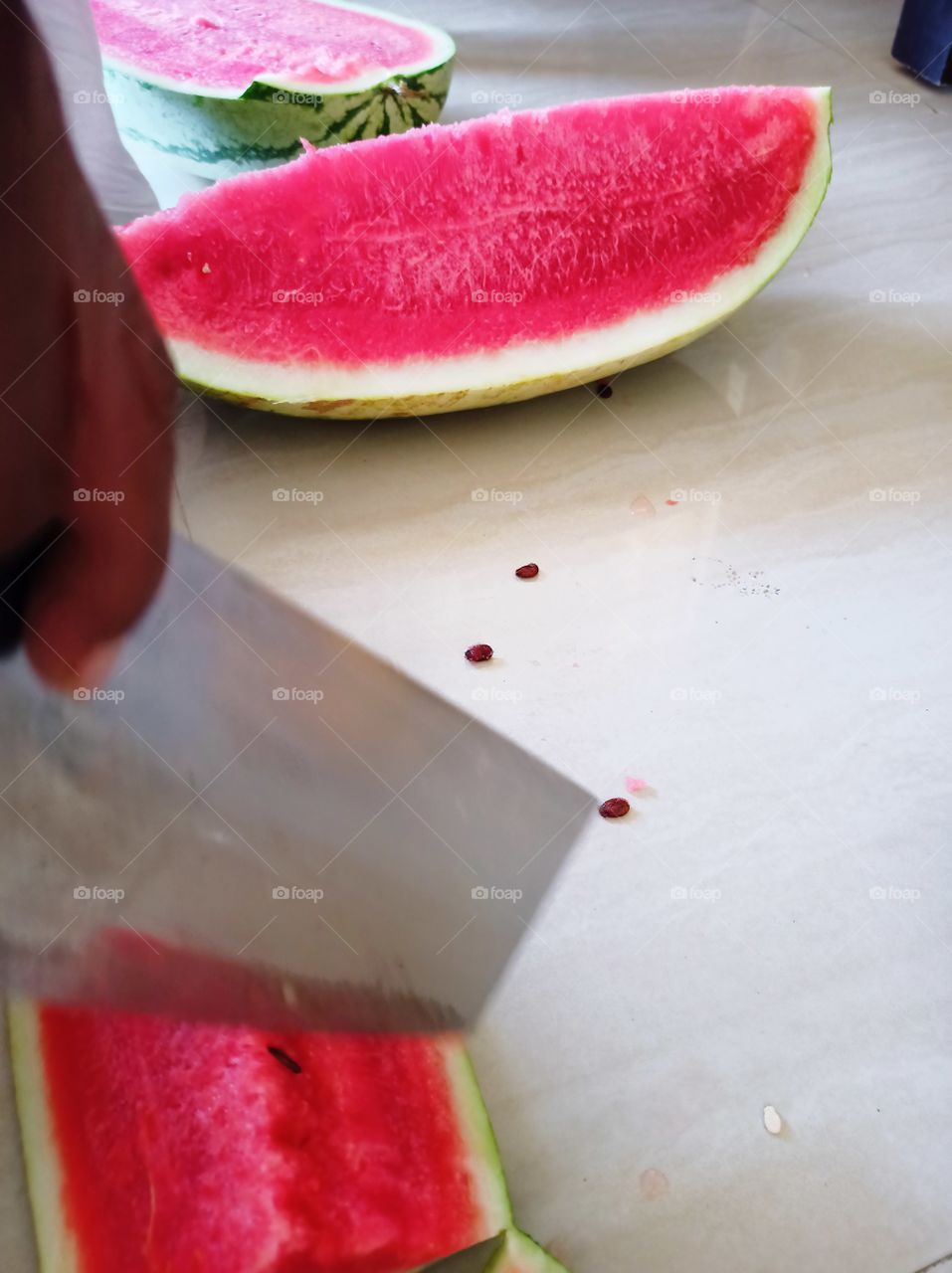 a middle-aged man is cutting summer season fruit water melon 🍉 🍉🍉 for the family members at home with chef knife