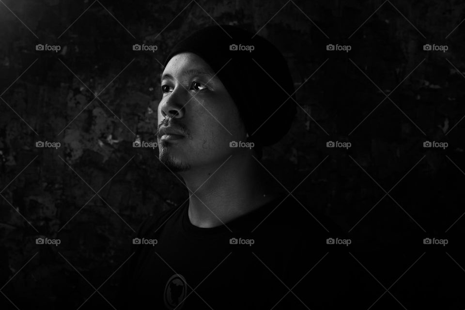 Black and white self-portrait of an Asian man wearing a beanie with a blank stare ahead.