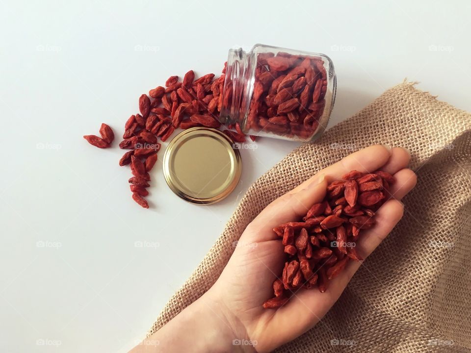 Goji berries on the hand and in the jar. Because of the light background, red berries get all attention in the picture. 