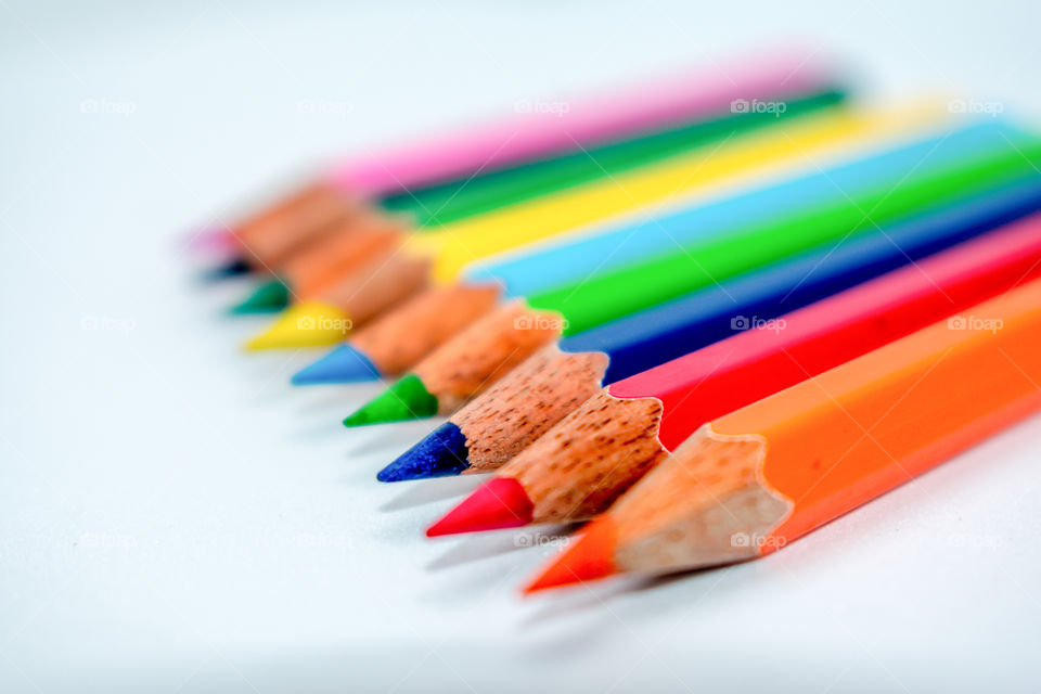 Standing Out From The Crowd Concept. Bunch of assorted multi colored pencils crayons in rainbow arrangement on white background, flat lay. Geometry pattern art design. Selective focus, blur image.