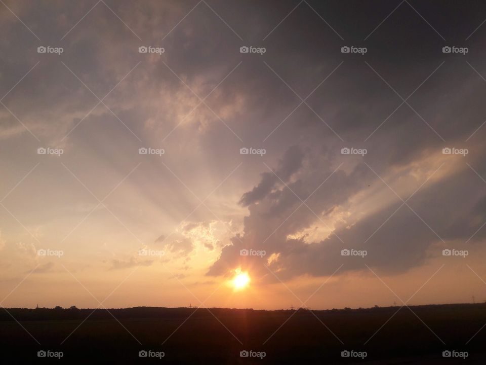 Sunset with a sun partly behind clouds and many rays of sunlight shines over the hole sky