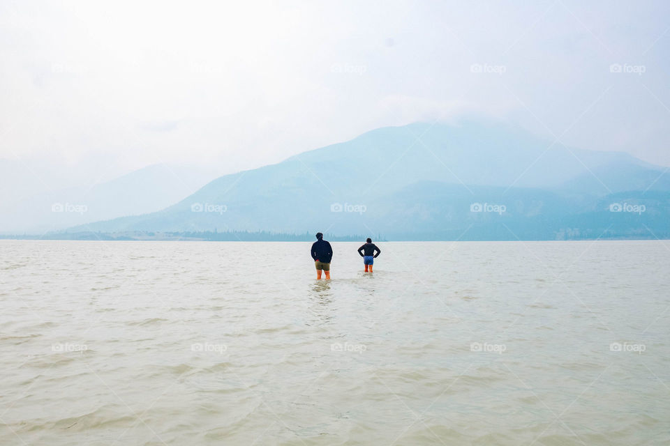 walking into the middle of a baby blue lake in Alberta Canada with smoky mountains in the background