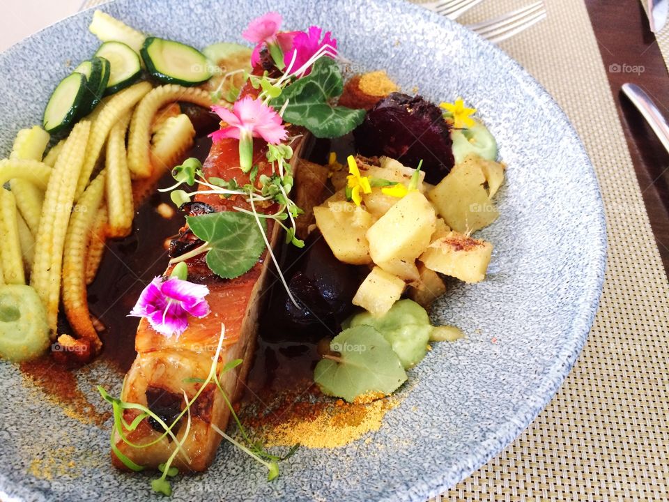 Grilled pork belly surrounded by colorful assortment of vegetables and edible flowers at an upmarket restaurant 