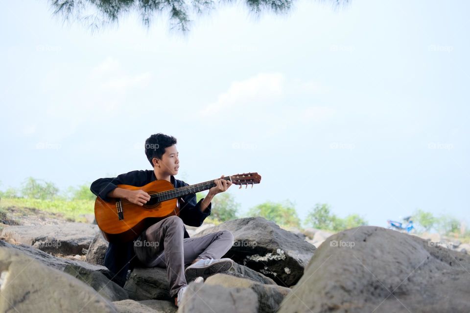 young man playing guitar under the tree