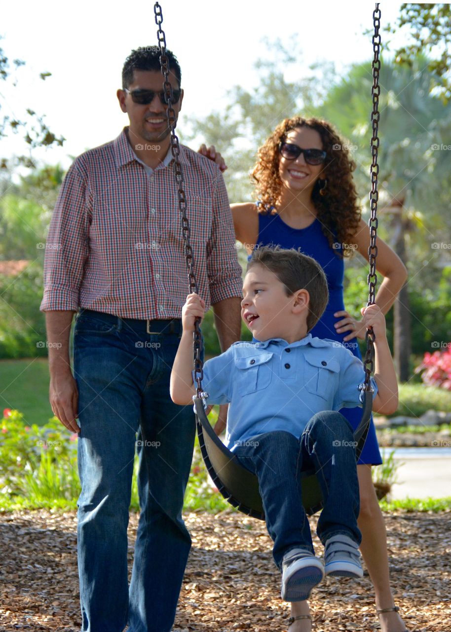 Mother and father standing near boy enjoying swing in playground