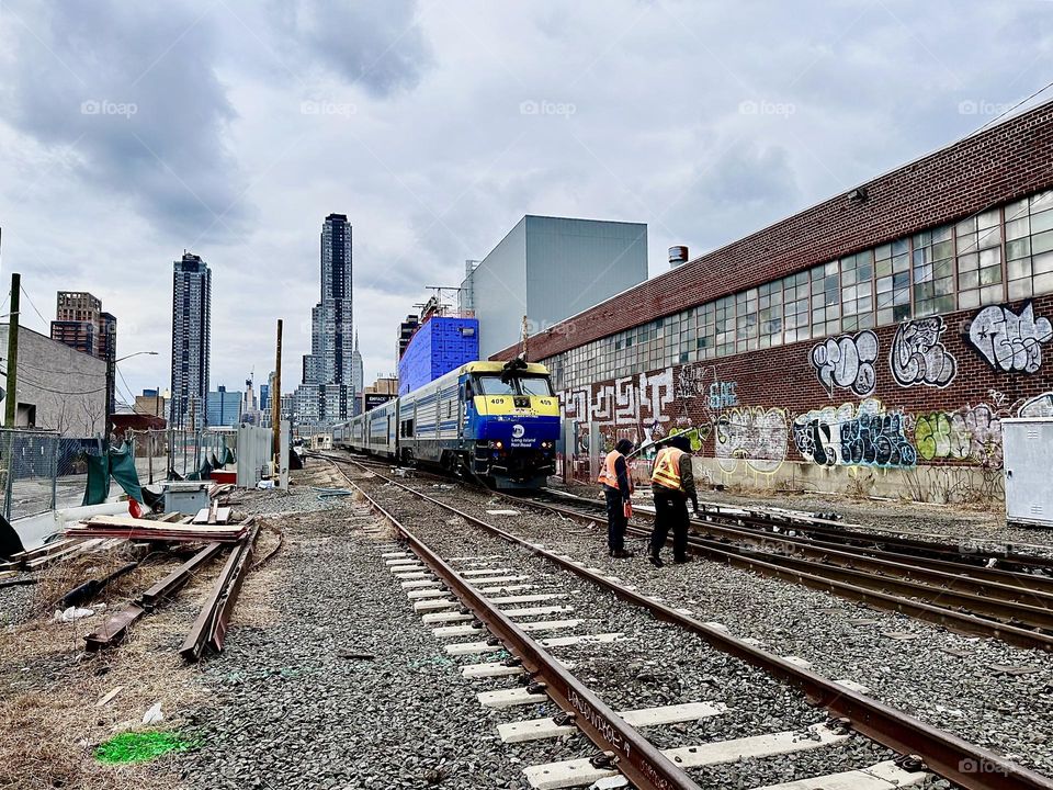 The „Long Island Railroad“ train is disappearing into the distance at „Borden Avenue“ and „11th Street“ by the „Pulaski Bridge“ at „Newtown Creek“ in LIC, Queens and the maintenance workers are already on the job again. 2023. Hypnotic Productions
