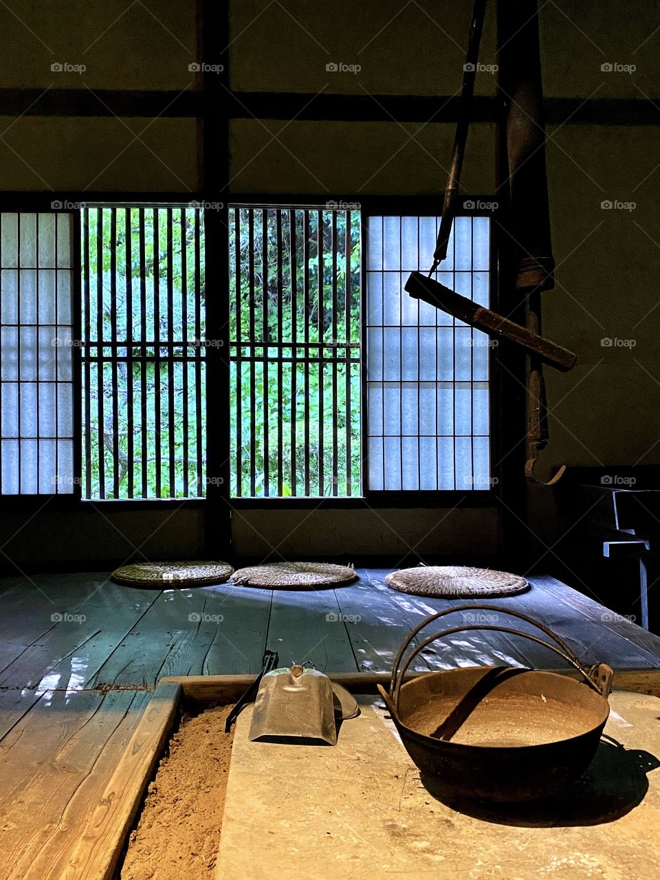 Light and shadows through windows with traditional Japanese paper blinds, straw mats and an irori fireplace in the foreground. 