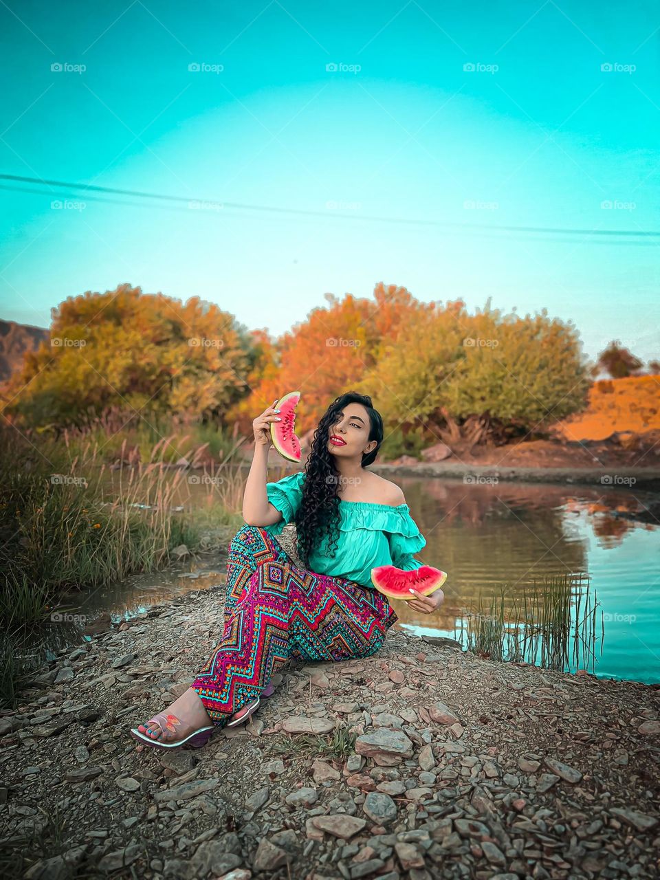 Curly-haired girl holding a watermelon by the lake