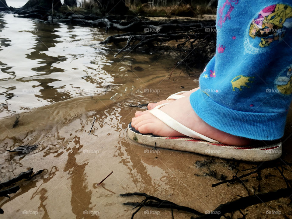 The feet of little girl in red white and blue flip flops standing in the sand at the very edge of the water at Jordan Lake near Apex North Carolina, Raleigh Triangle area. Patriotic. 
